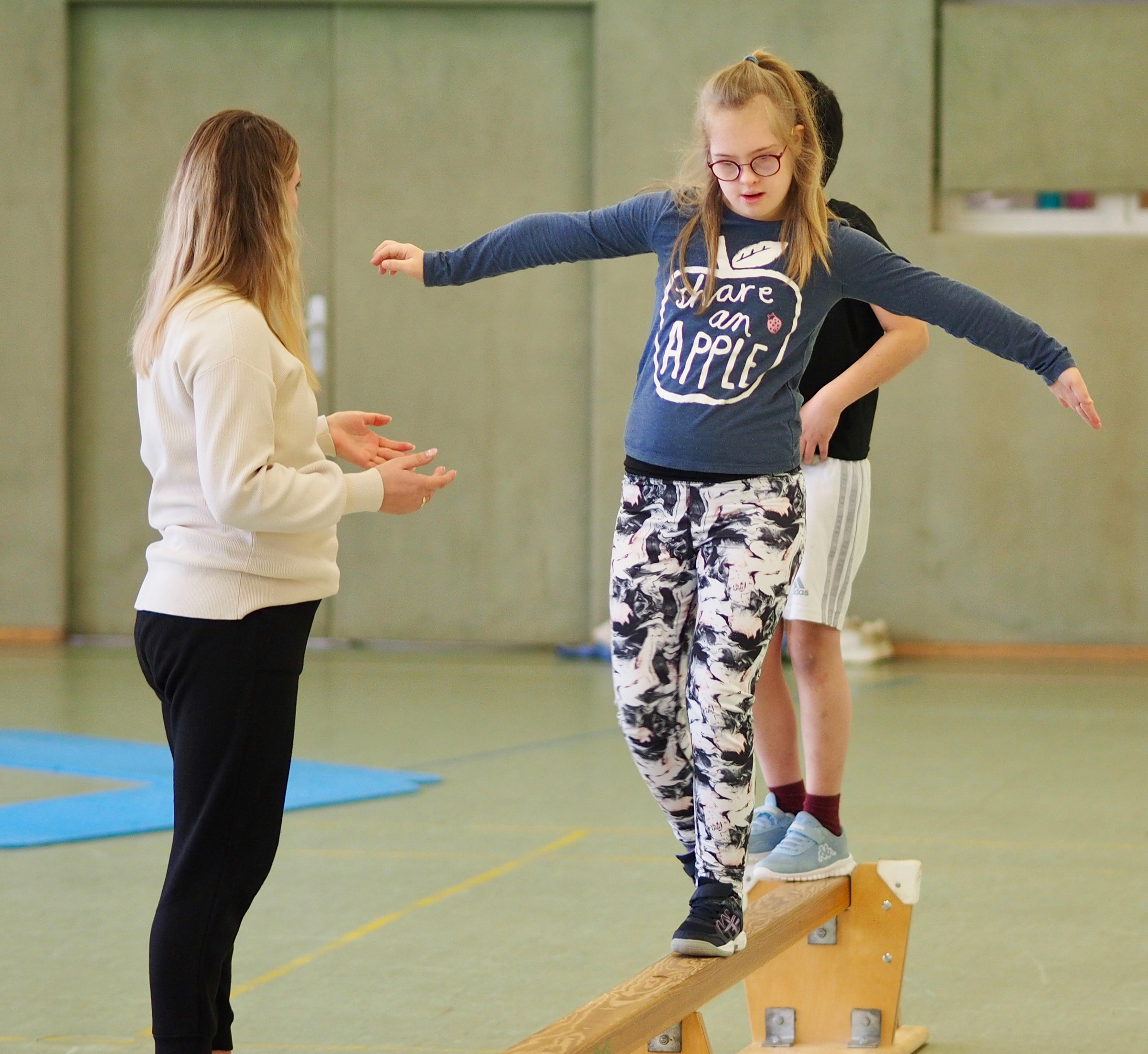 Kind wird im Sportunterricht von einem Mitarbeitenden unterstützt